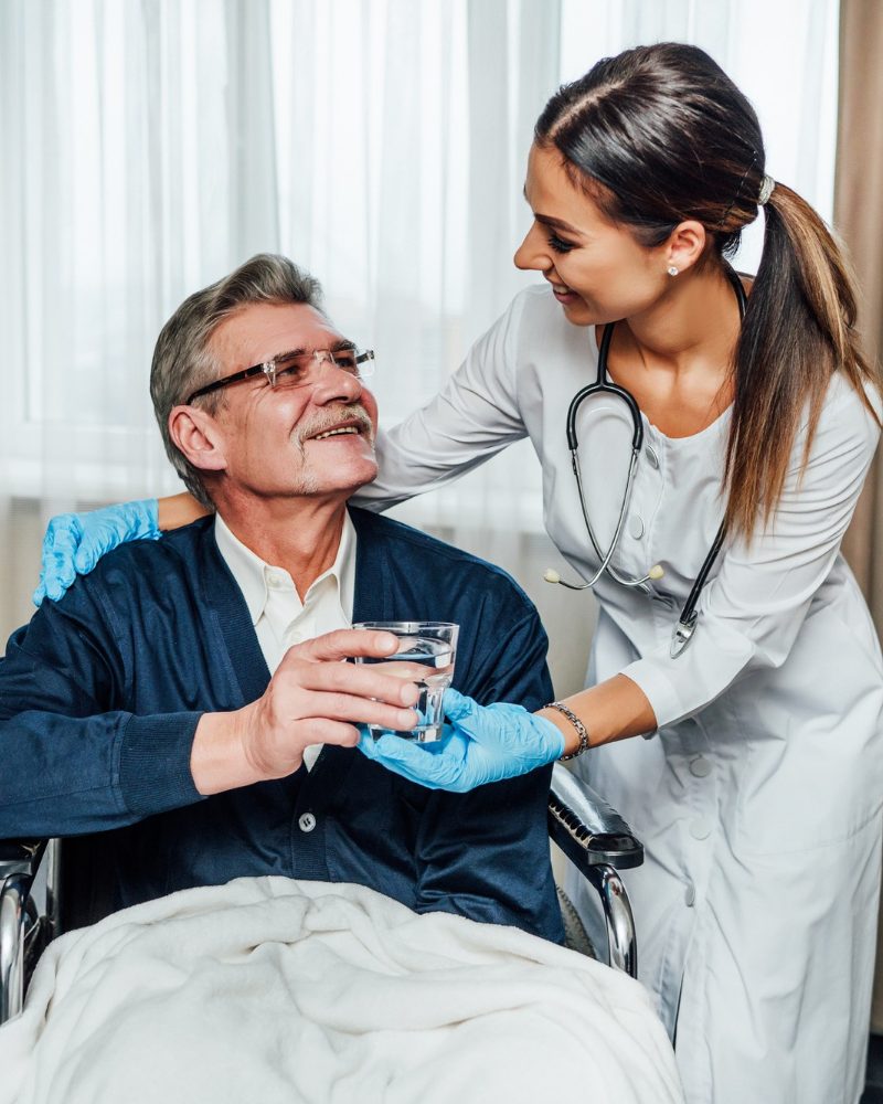 older-man-wheelchair-smiles-nurse-assistant-she-hands-him-glass-water
